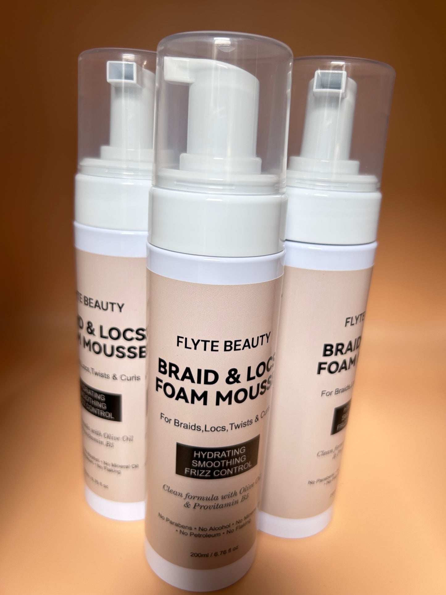Three bottles of Flyte Beauty Braid & Locs Foam Mousse on a gradient background