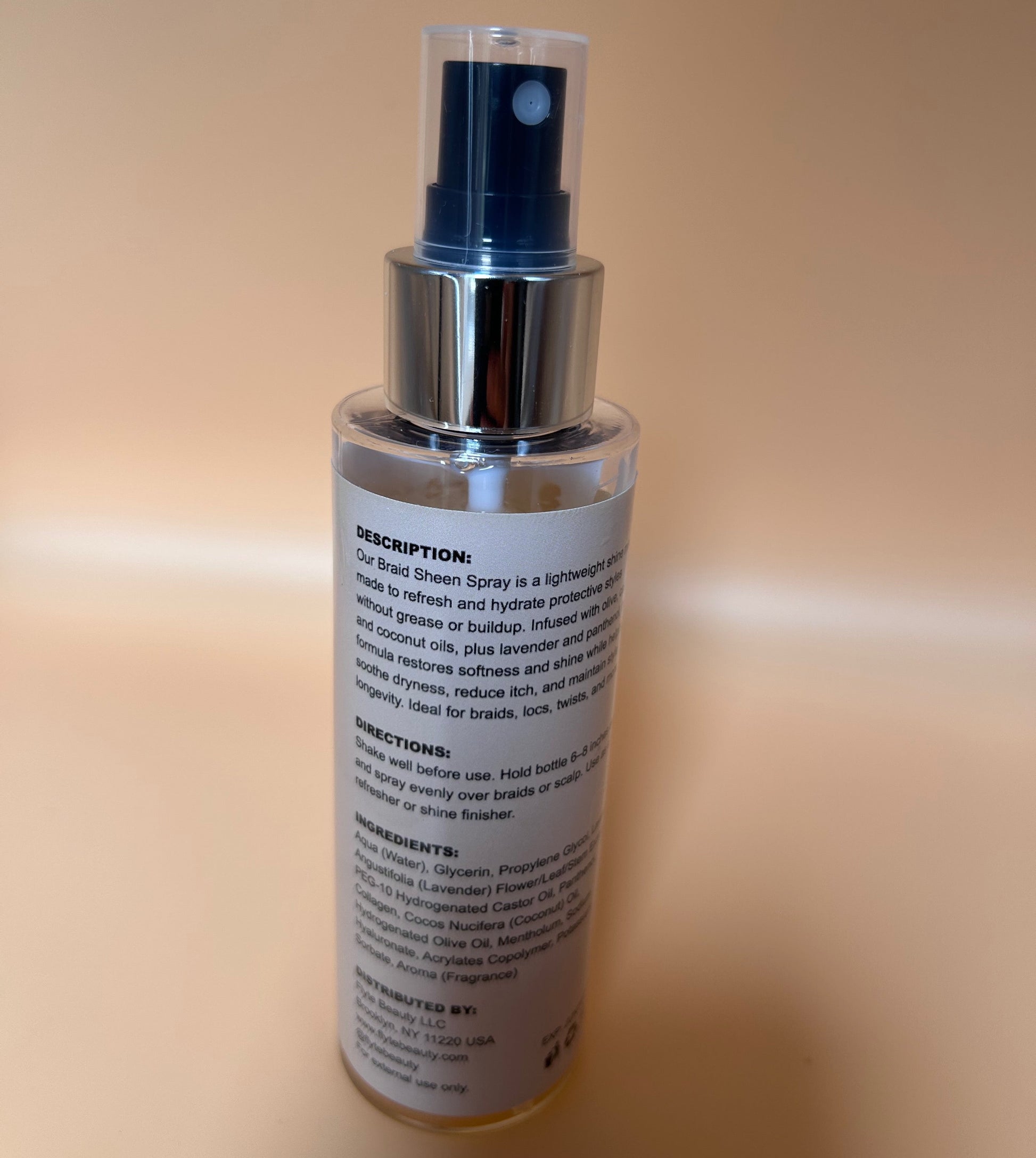 Clear spray bottle with silver nozzle on a beige background
