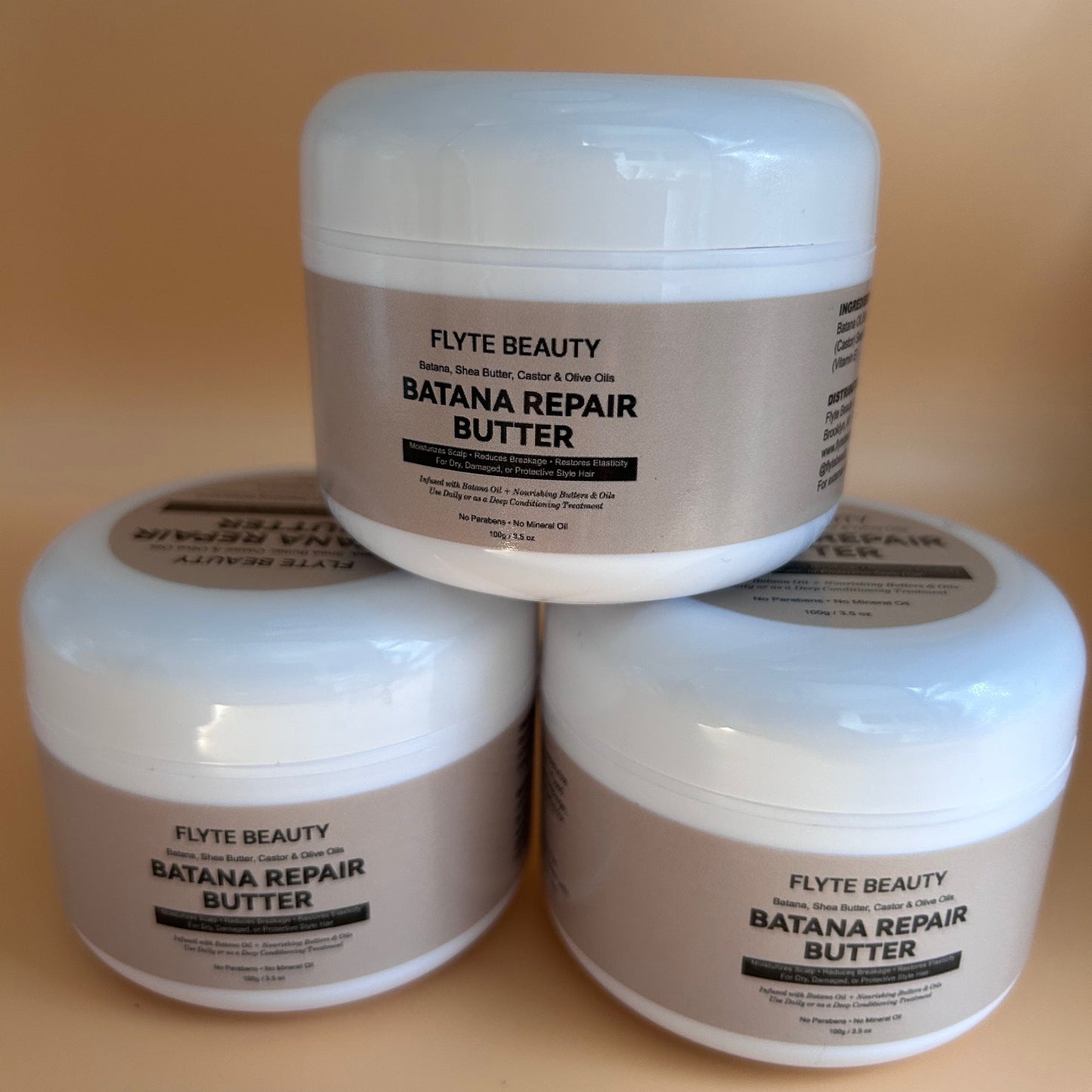 Three jars of Flyte Beauty Batana Repair Butter stacked on a beige background